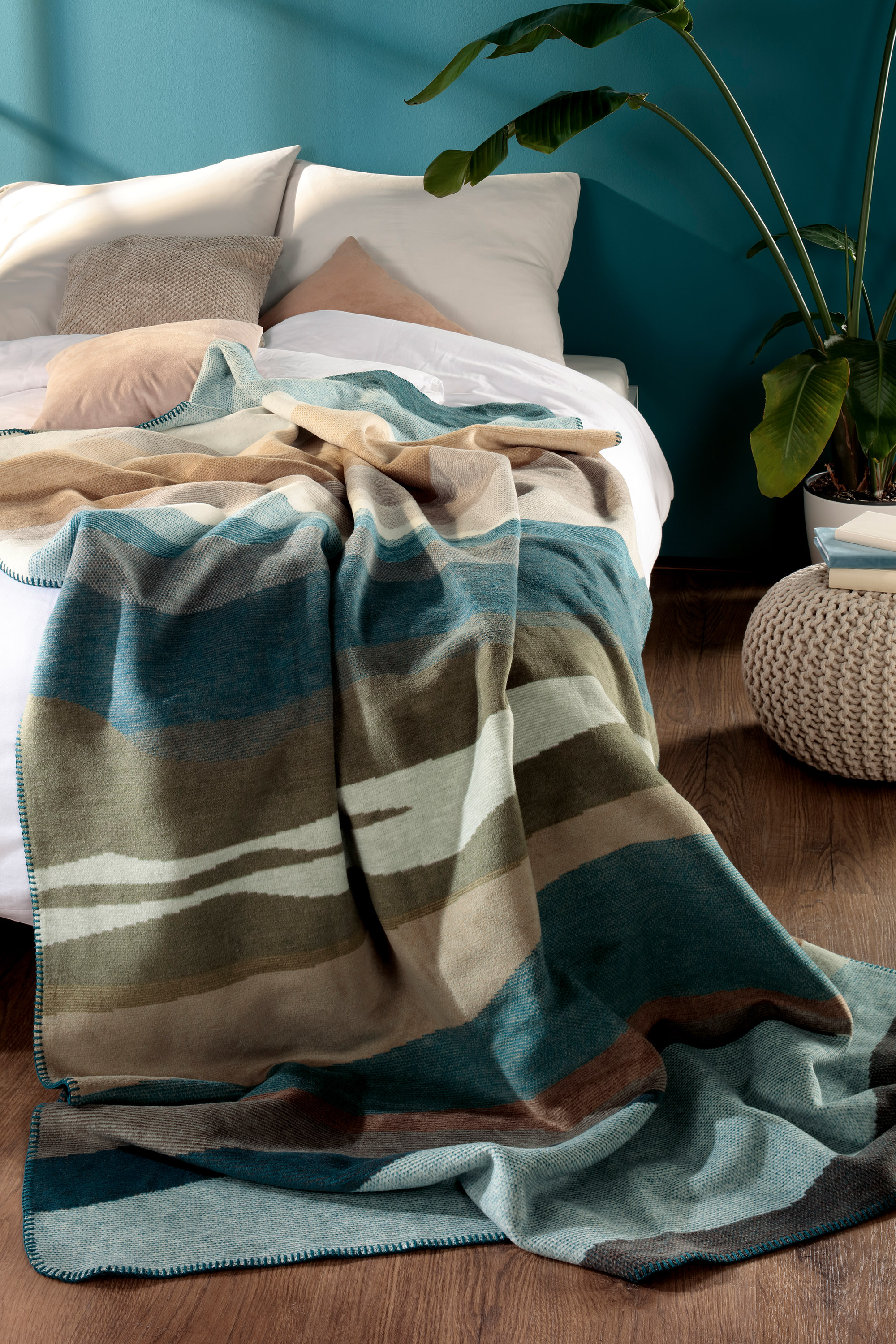 Wohndecke Blue Fade auf Bett mit Pflanze im Hintergrund