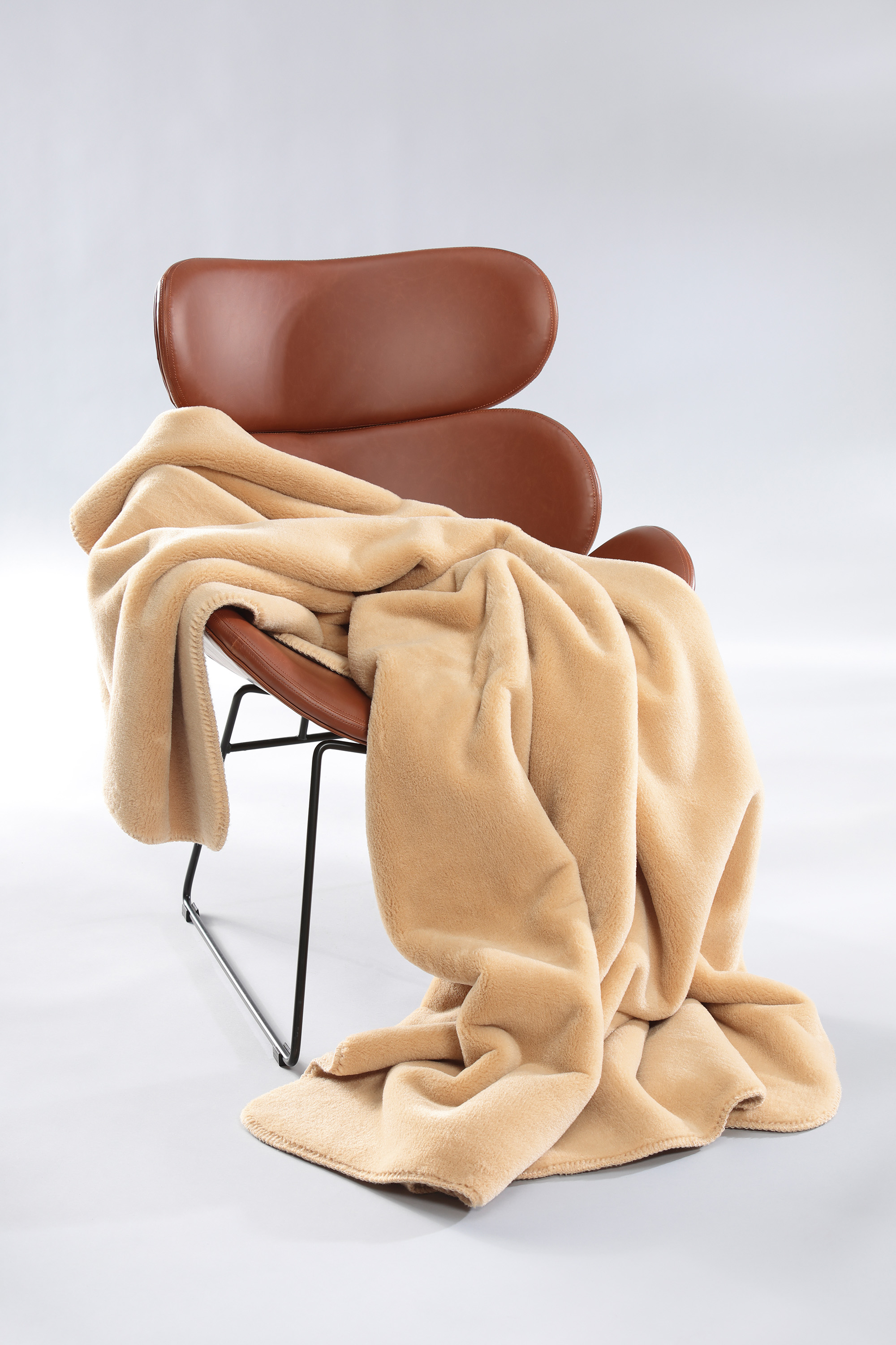 Wohndecke Wool Feel camel auf Sessel gelegt