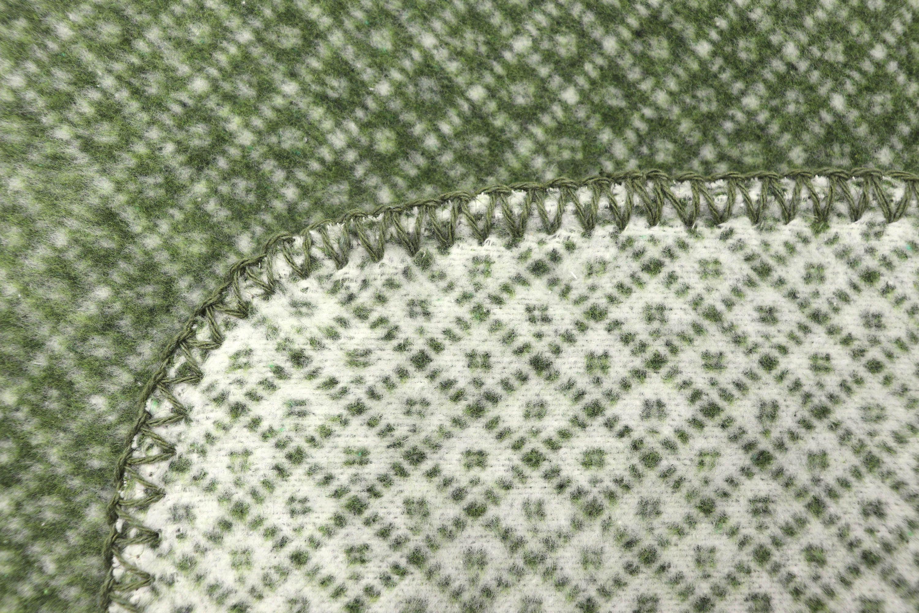 Nachhaltige Kuscheldecke "Tiny green" aus Recycling-Garn mit minimalem Muster in grün - Detailaufnahme Einfassung